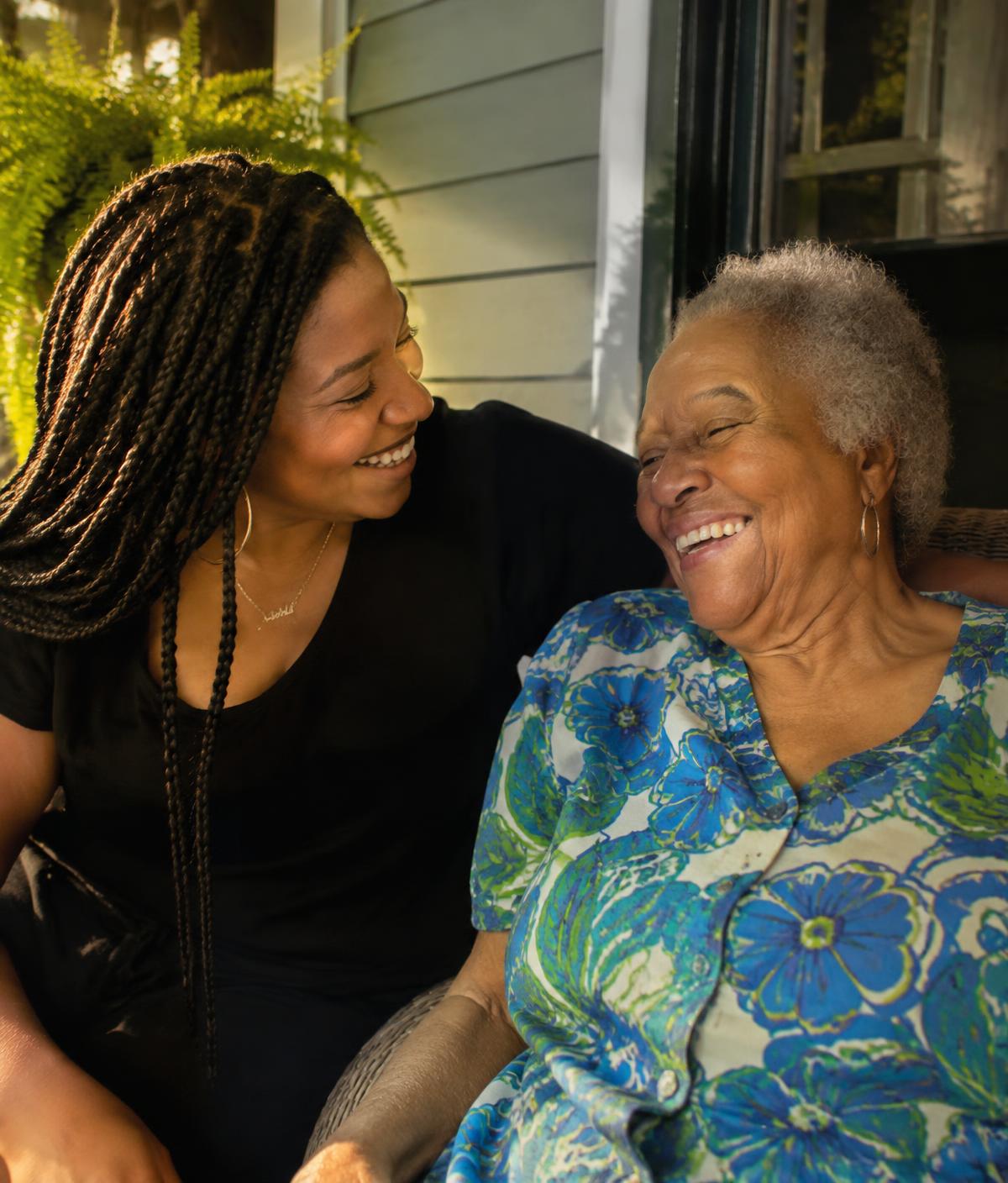 An adult daughter laughing with her mother on a porch (illustrative photo)